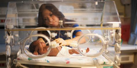 NICU nurses in scrubs standing around an incubator